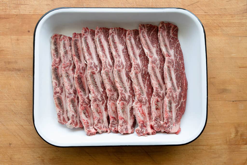 uncooked kalbi or short ribs in a pan on a cutting board
