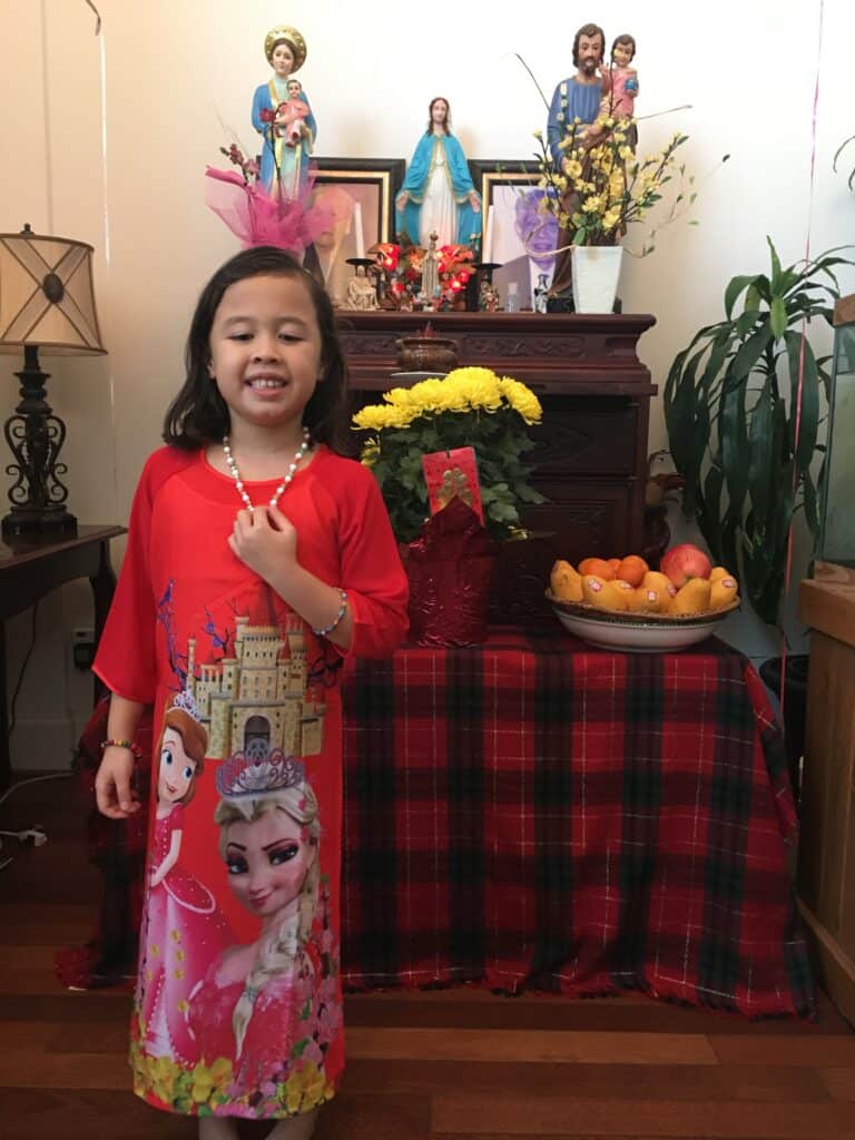 My daughter in a traditional Vietnamese Áo dài in front of an alter my mom decorated with fruits, fresh flowers, incense, and a picture of my maternal grandparents.